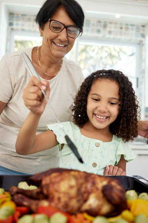 Kitchen, food and a grandmother cooking with her grandchild in their home together for thanksgiving. Children, love and a roast with a senior woman preparing a meal with a girl for healthy nutritionの写真素材