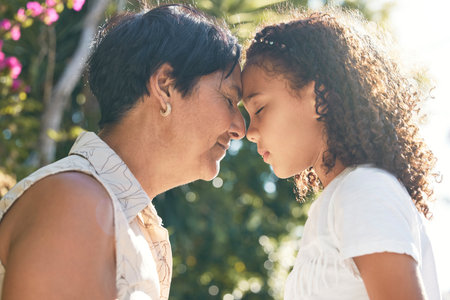 Grandmother, girl and forehead together in garden with eyes closed, connection and bonding with love in summer. Woman, female child and face touch with care, family and relax in sunshine on holidayの写真素材