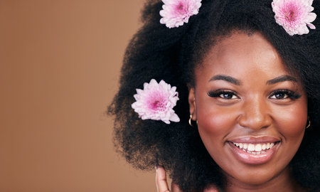 Flowers, face and black woman in afro hair care, smile and beauty in studio isolated on a brown background mockup space. Portrait, floral hairstyle cosmetic and natural African model in organic salonの写真素材