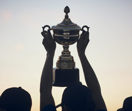 Sunset, trophy in hands and silhouette and team with sports, athlete group and people outdoor with celebration. Winning, club and success with prize, reward and bonus, sky and support and achievementの写真素材