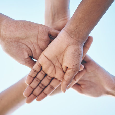 Blue sky, hands stack and together for team building motivation, group cooperation or community goals support. Closeup below view, synergy commitment and people collaboration, teamwork and solidarityの写真素材