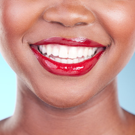 Woman, smile and red lipstick with teeth and beauty, dental and makeup closeup isolated on blue background. Model with bold cosmetic product on lips, dental and mouth with skin and shine in studioの写真素材
