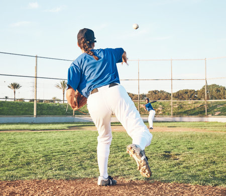 Baseball, pitching and a sports person outdoor on a pitch for performance or competition. Behind professional athlete or softball player with fitness, ball and throw for game, training or exerciseの写真素材