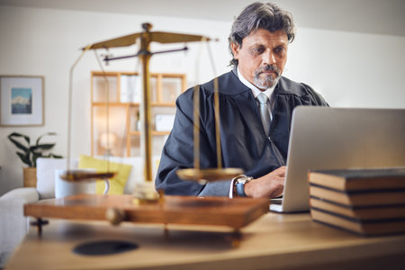 Scales, justice and man in office with laptop for working in law firm, court research or search online for legal policy or rules. Judge, attorney or mature businessman with communication on computerの写真素材