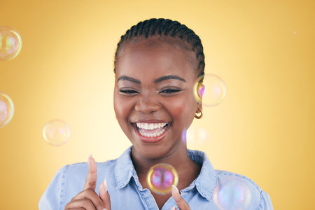 Excited, pop and black woman on yellow background with bubbles for happiness, joy and fun. Playful, smile and isolated happy African person in studio with soap bubble for freedom, magic or colorの写真素材