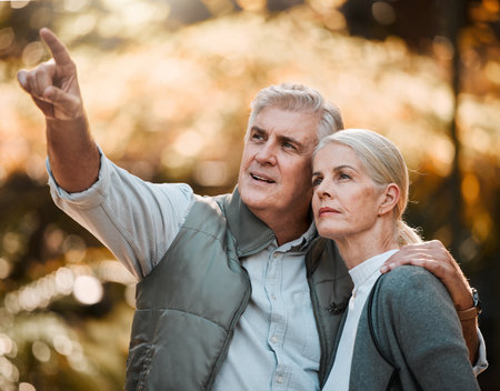 Senior couple, outdoor hiking and pointing with thinking, view or direction in nature, sunshine or adventure. Elderly man, woman and together with vision, walk or check environment on holiday in parkの写真素材