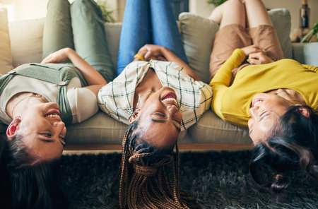 Upside down, friends and relax on sofa together with head hanging on couch and smile with happiness in home on weekend. Group, diversity and women laughing in fun, bonding or laying on chair in houseの写真素材
