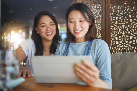 Restaurant, tablet and Asian women for menu, food options and online order for lunch, meal or dinner. Coffee shop, cafe and happy friends on digital tech for social media review, website and appの写真素材