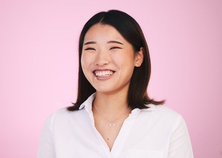 Portrait, happy and asian woman laugh in studio with funny, joke or silly humor on pink background. Comic, smile and face of female model laughing to goofy, comedy or playful, good mood or positivityの写真素材