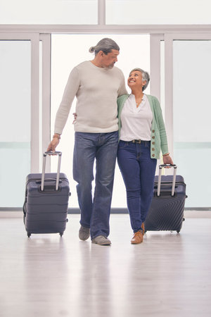 Mature couple, suitcase and walking in airport lobby, happy and travel together on tourist holiday. Man, woman smile and luggage for flight on vacation, immigration journey and global airplane tripの写真素材