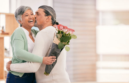 Mature couple, flowers and kiss at home for anniversary, birthday or valentines celebration. Surprise, love and roses bouquet with a man and woman for healthy marriage, happiness and mockup spaceの写真素材