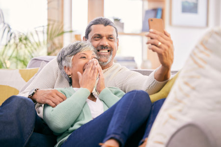 Happy, selfie and a senior couple with a phone on the sofa for communication, social media or a video call. Smile, house and an elderly man and woman taking a photo with a mobile on the couchの写真素材