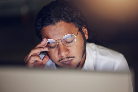 Businessman, headache and stress at computer at night in office working late on deadline. Tired entrepreneur person with glasses and hands on head for pain, burnout or depression and fatigue at workの写真素材