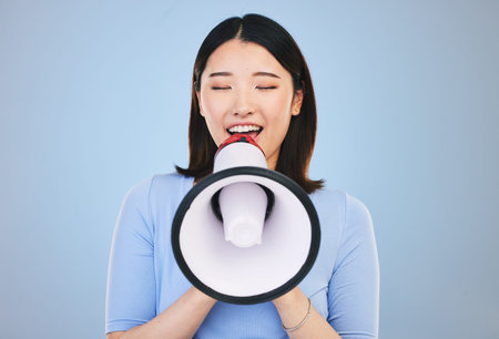 Woman, megaphone and voice for news, broadcast or student sale and announcement on blue background. Young asian person with noise for call to action, university attention or college speaker in studioの写真素材