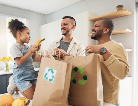 Shopping, bags and happy family with groceries in home and girl with fruit and gay parents, dad and father in kitchen. Sustainable, paper bag and people with eco friendly grocery, product or fruitsの写真素材