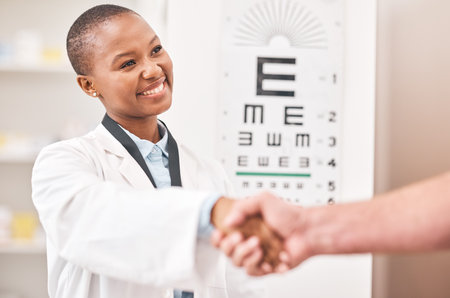 Optometrist woman, handshake and smile with patient, customer and happy for agreement, deal or sale. African ophthalmology doctor, shaking hands and kindness for healthy eyes, wellness or healthcareの写真素材