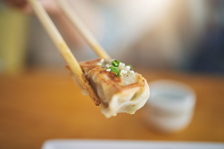 Closeup, protein and chopsticks with dumpling at a restaurant for food, Asian culture or fine dining. Health, hungry and person with dinner, eating lunch or enjoying a fried dish or cuisine at a cafeの写真素材