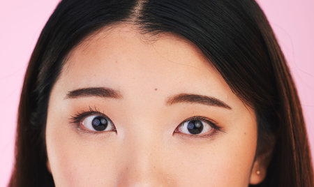 Closeup, eyes and portrait of an Asian woman on a pink background for makeup or microblading. Face,...