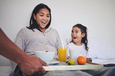 Surprise, breakfast and mother with child in bed relaxing on weekend morning at their home. Happy, smile and young mom enjoying healthy food for brunch meal with her daughter for mothers day in houseの写真素材