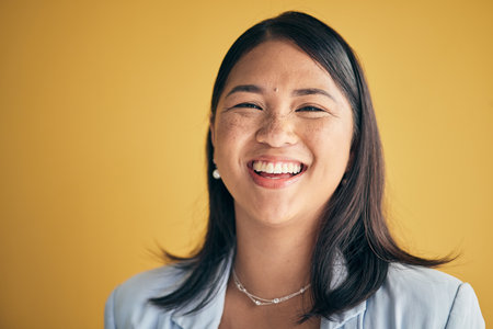 Face, happy and Asian woman, designer and entrepreneur in studio isolated on a yellow background mockup space. Portrait, funny and creative professional, worker laugh and startup employee in Cambodiaの写真素材