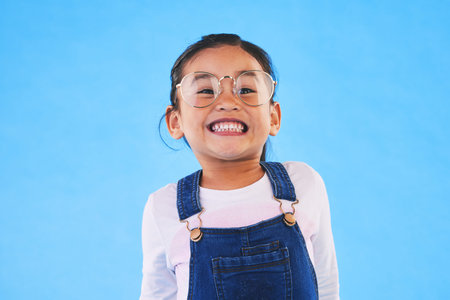 Girl kid, glasses and vision in studio with smile, medical and thinking for eye care by blue...