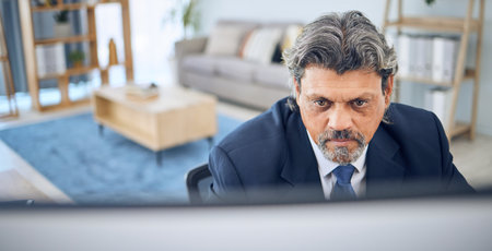 Mature businessman, reading and computer in home, apartment or corporate employee with remote work in lounge. Distance, working and manager with project, report or review on pc in house officeの写真素材