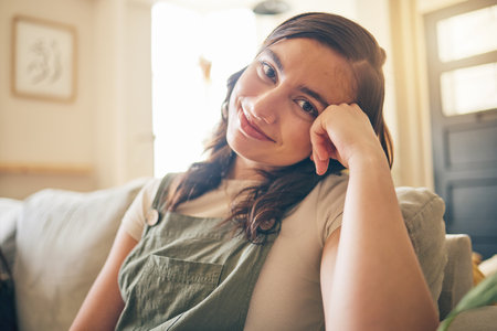 Happy, smile and portrait of woman on a sofa relaxing in the living room of her apartment. Calm, peaceful and face of young female person from Canada with positive attitude sitting in lounge at home.の写真素材