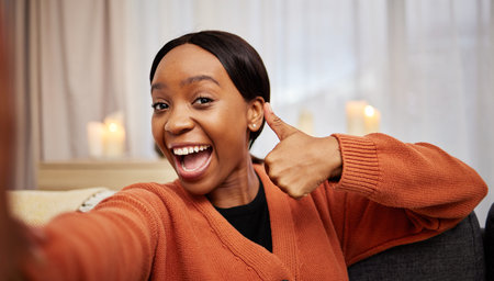 Selfie, black woman and thumbs up at home with a smile for success, motivation and excited. Portrait, happy and African female person in a living room with a like, yes and emoji hand sign at houseの写真素材