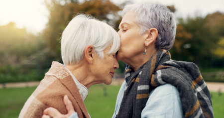 Senior woman kissing her friend on the forehead for affection, romance and bonding on outdoor date....