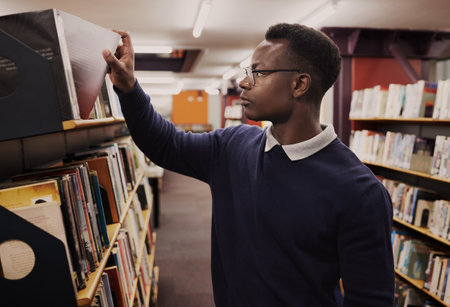 University, books and black man in a library reading and learning on campus for knowledge and education in college. Smart, clever and person doing research or studying by a shelf for an examの写真素材