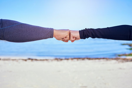 Fitness, couple and fist bump on the beach for exercise, outdoor workout or celebration in water sports, teamwork and cardio. People, hands and sign of collaboration together in support or successの写真素材