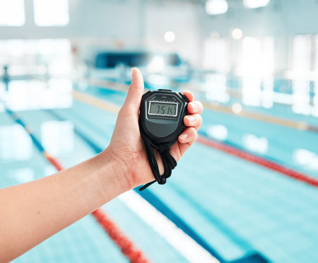 Person, hand and stopwatch by pool in swimming, race or sports training in fitness, exercise or workout. Closeup of swim coach holding timer for monitoring performance, speed or setting challengeの写真素材
