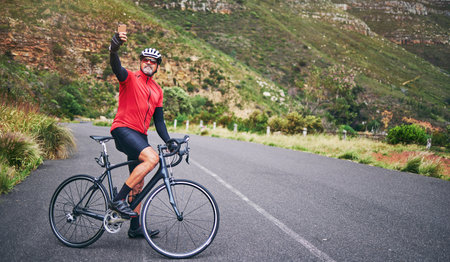 Selfie, mountain and man cycling for exercise, training and workout goals in nature for social media. Sports, travel blog and male cyclist take picture for wellness, cardio and fitness on adventureの写真素材