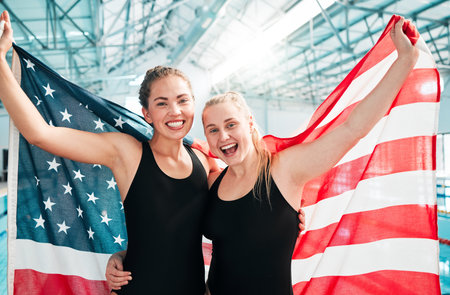 Athlete women, american flag and celebration for win, fitness or excited smile in portrait at sports contest. Girl team, winner and hug by swimming pool for success, exercise and goals at competitionの写真素材