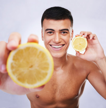 Beauty, lemon and offer with portrait of man in studio for health, detox and cosmetics. Vitamin c, nutrition and summer with face of person and fruit on white background for self care and skincareの写真素材
