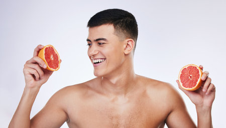 Beauty, grapefruit and health with face of man in studio for skincare, detox and natural cosmetics. Vitamin c, nutrition and summer with person and fruit on white background for self care and glowの写真素材