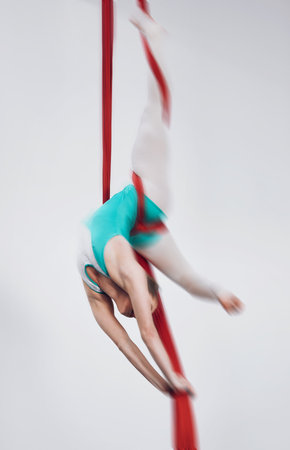 Sport, acrobat and aerial silk with a woman in air for performance, gymnastics and balance. Young athlete person or gymnast hanging on red fabric and white background with space, art and creativityの写真素材