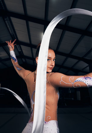 Woman, portrait and ribbon gymnastics in dance competition, performance and concert in dark arena. Elegant dancer, rhythm and athlete training with talent for creative movement, contest and skillの写真素材