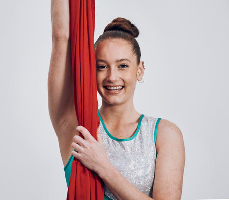 Portrait, ribbon dancer and competition with a woman in studio on a gray background for routine training. Fitness, smile and energy with a happy athlete holding fabric for a performance showcaseの写真素材