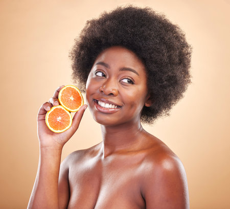 Orange, natural skincare and woman on studio background for healthy cosmetics, vegan benefits or nutrition. Happy african beauty model thinking of citrus fruits for vitamin c, diet or eco dermatologyの写真素材