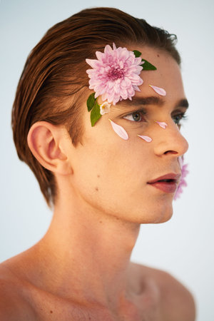 Beauty, petals and flowers on face of man in studio for spring, natural cosmetics and creative. Glow, self love and floral with model on white background for makeup, spa treatment and wellnessの写真素材