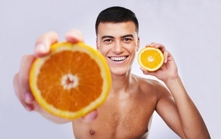 Happy man, portrait and orange in vitamin C, diet or skincare against a white studio background. Male person or model smile with organic citrus fruit for natural nutrition, health and wellnessの写真素材