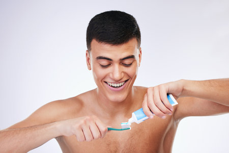 Happy man, toothbrush and toothpaste for cleaning teeth in dental care hygiene or grooming against a white studio background. Male person smile for tooth whitening, oral or gum and mouth treatmentの写真素材