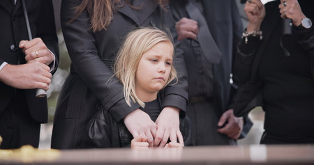 Child, sad and family at funeral at graveyard ceremony outdoor at burial place. Death, grief and group of people with casket or coffin at cemetery for service while mourning a loss at event or graveの写真素材