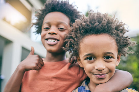 Kids, portrait and hug with thumbs up in a backyard for brothers, bonding and fun outdoor. Black family, love and face of children in a garden embrace with hand emoji, gesture or yes sign on weekendの写真素材