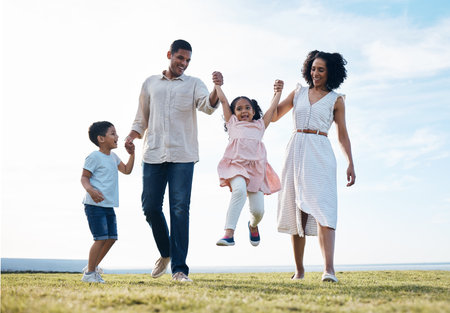 Family, holding hands and outdoor at a park with love, care and happiness together in nature. Young man and woman or parents swing children on walk, travel and playing on fun journey or holidayの写真素材