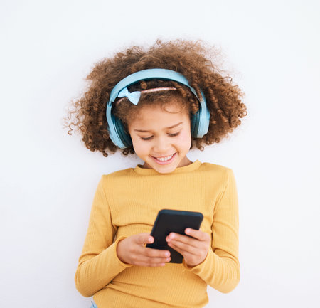 Girl kid, chat and smartphone, headphones and music with smile isolated on white background....