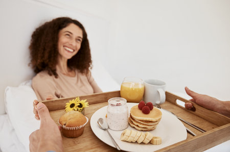 Breakfast, romance and woman in bed for surprise, anniversary celebration and special birthday. Morning, love and happy couple with food, pancake and juice on tray for wellness, nutrition and hungerの写真素材