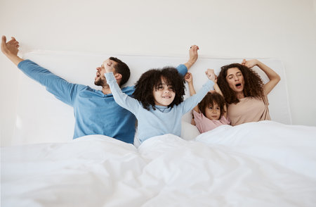 Family, bed and yawn in morning wake up, relax or sleep together with arms up at home. Calm parents, children and bonding on holiday break, weekend or new day in peace, support or comfort in bedroomの写真素材