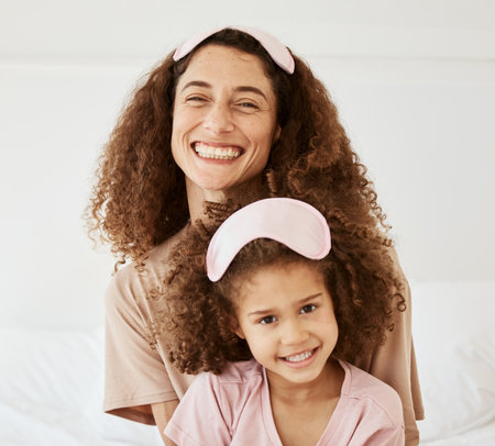 Mother, daughter and sleep mask, happiness in portrait and bonding with love and care in the morning. Woman, young girl and smile at home, pajamas and family, positivity and fun together in bedroomの写真素材